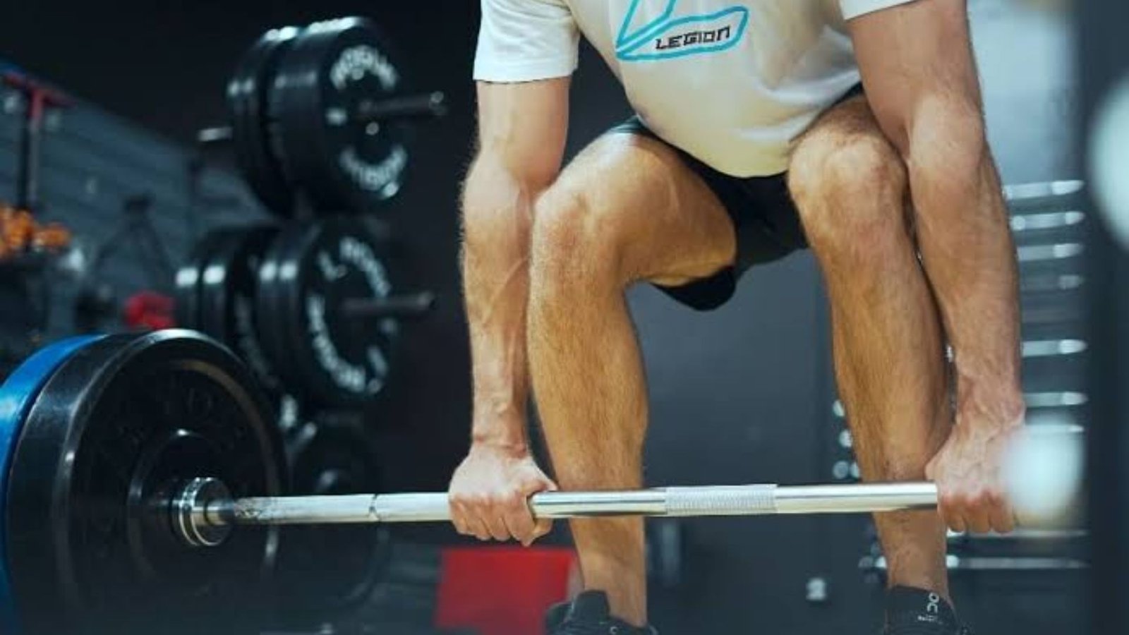 man setting up for a barbell deadlift in a gym with weight plates, demonstrating proper lifting position.