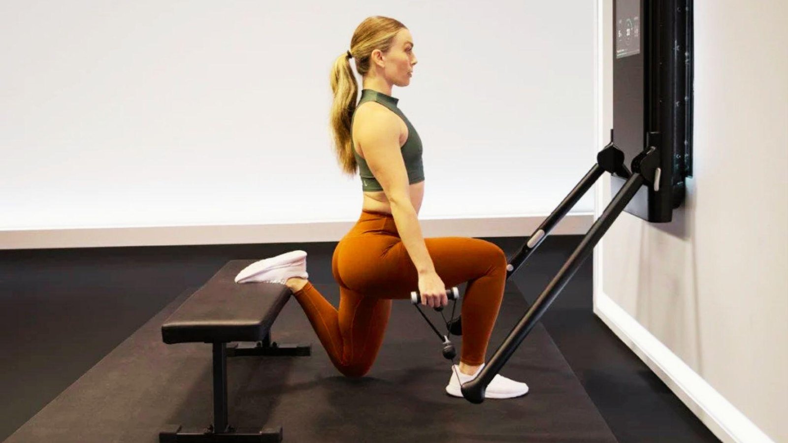 Woman in green crop top and brown leggings doing Bulgarian split squat with cable resistance and bench.
