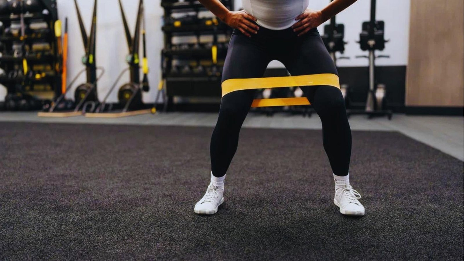 Person doing banded squat abduction with yellow mini resistance band around knees for glute activation.