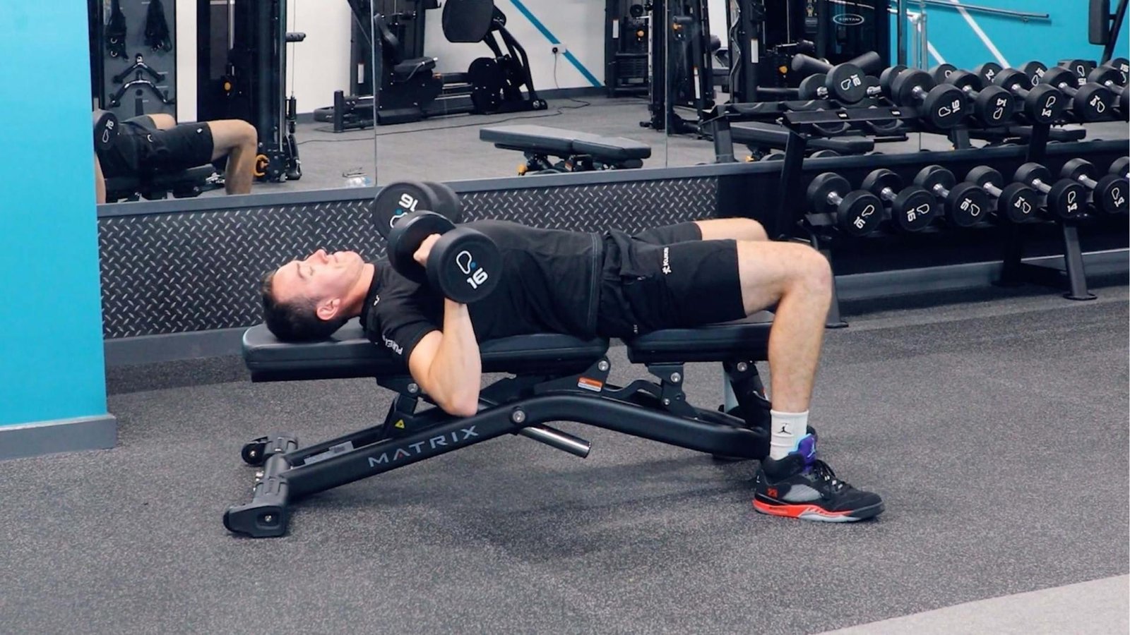 Man performing dumbbell bench press on flat bench with 16kg dumbbells, cause of shoulder pain.