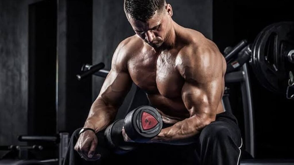 muscular man resting with a dumbbell after a medial delt workout in the gym.