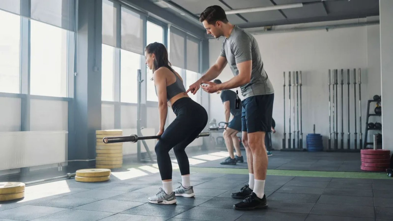 fitness coach correcting a woman's hip hinge form during a Romanian deadlift.