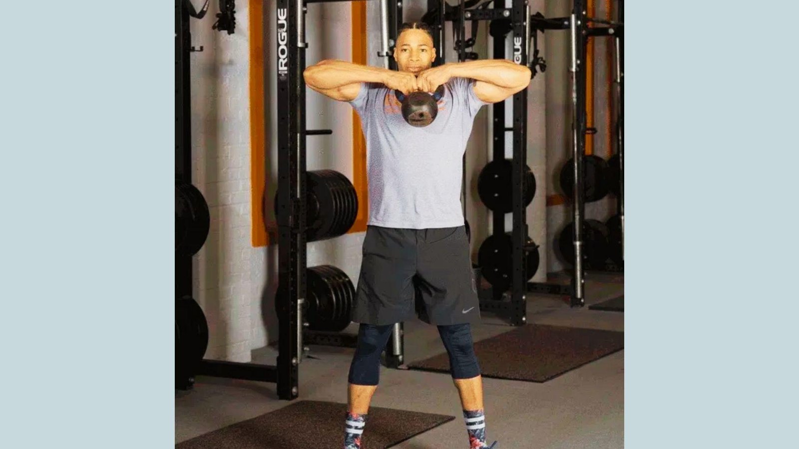 Man in gray shirt and black shorts doing a kettlebell high pull upright row in the weight room.