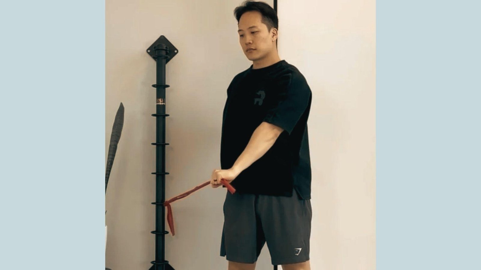 Man in black shirt doing standing resistance band row exercise attached to black wall-mounted pole.
