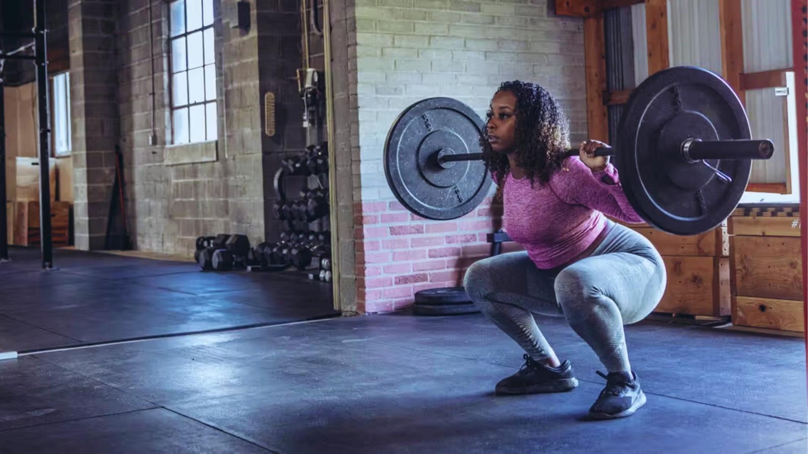 Woman doing barbell squat with heavy weight in CrossFit gym focusing on form.