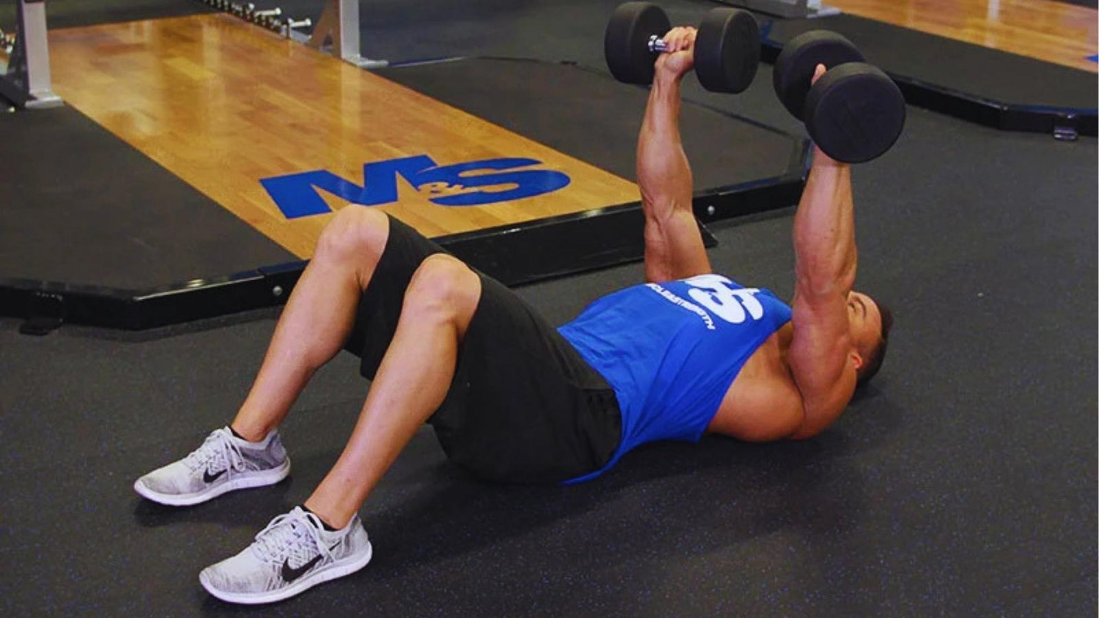 Muscular man doing dumbbell floor press with heavy dumbbells, shoulder-friendly bench press fix.
