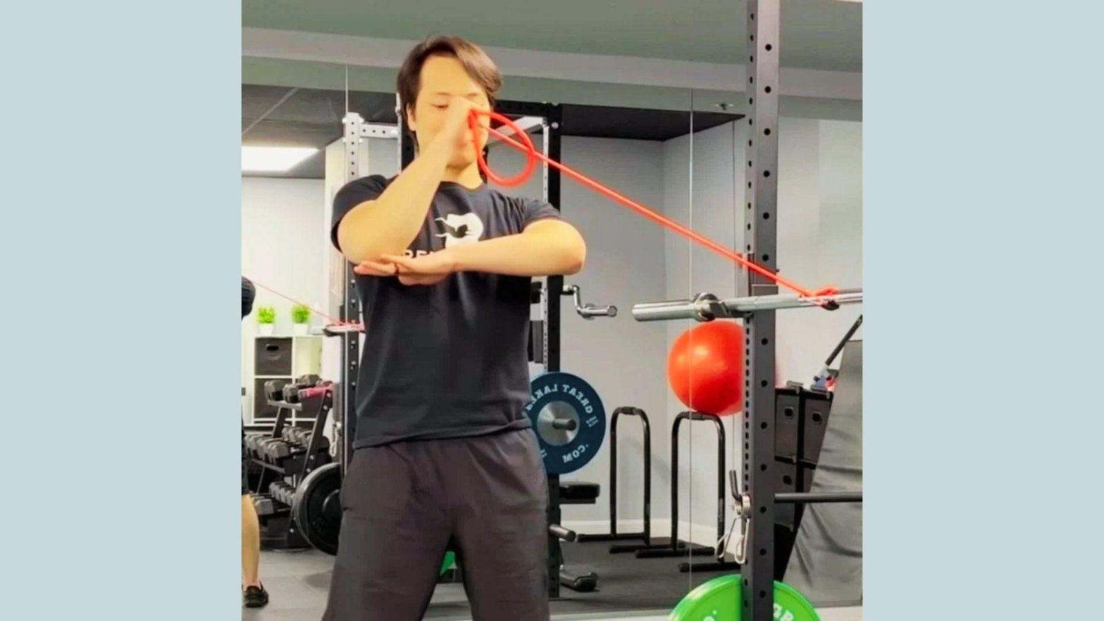 Man in black shirt doing standing resistance band internal rotation exercise anchored to rack in gym.