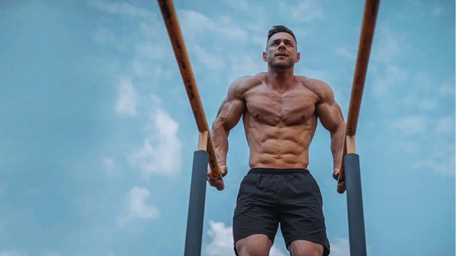 Muscular man doing chest dips on outdoor parallel bars showing triceps strength exercise.