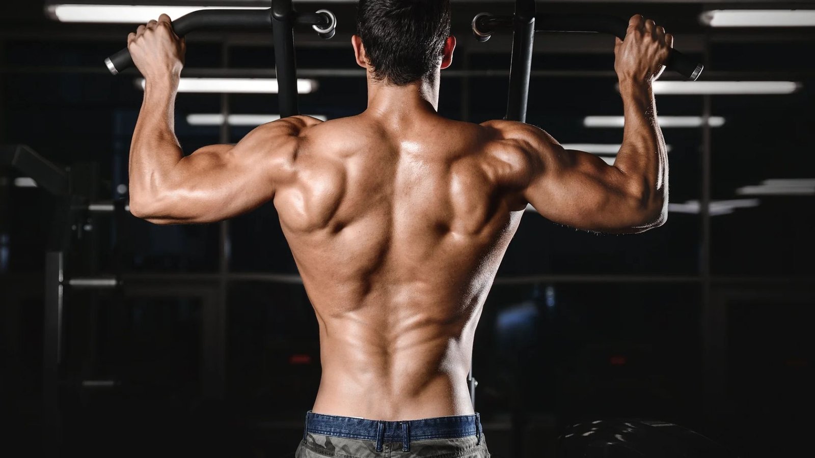 man performing pull-up showing broad shoulders and developed medial delts in a gym.