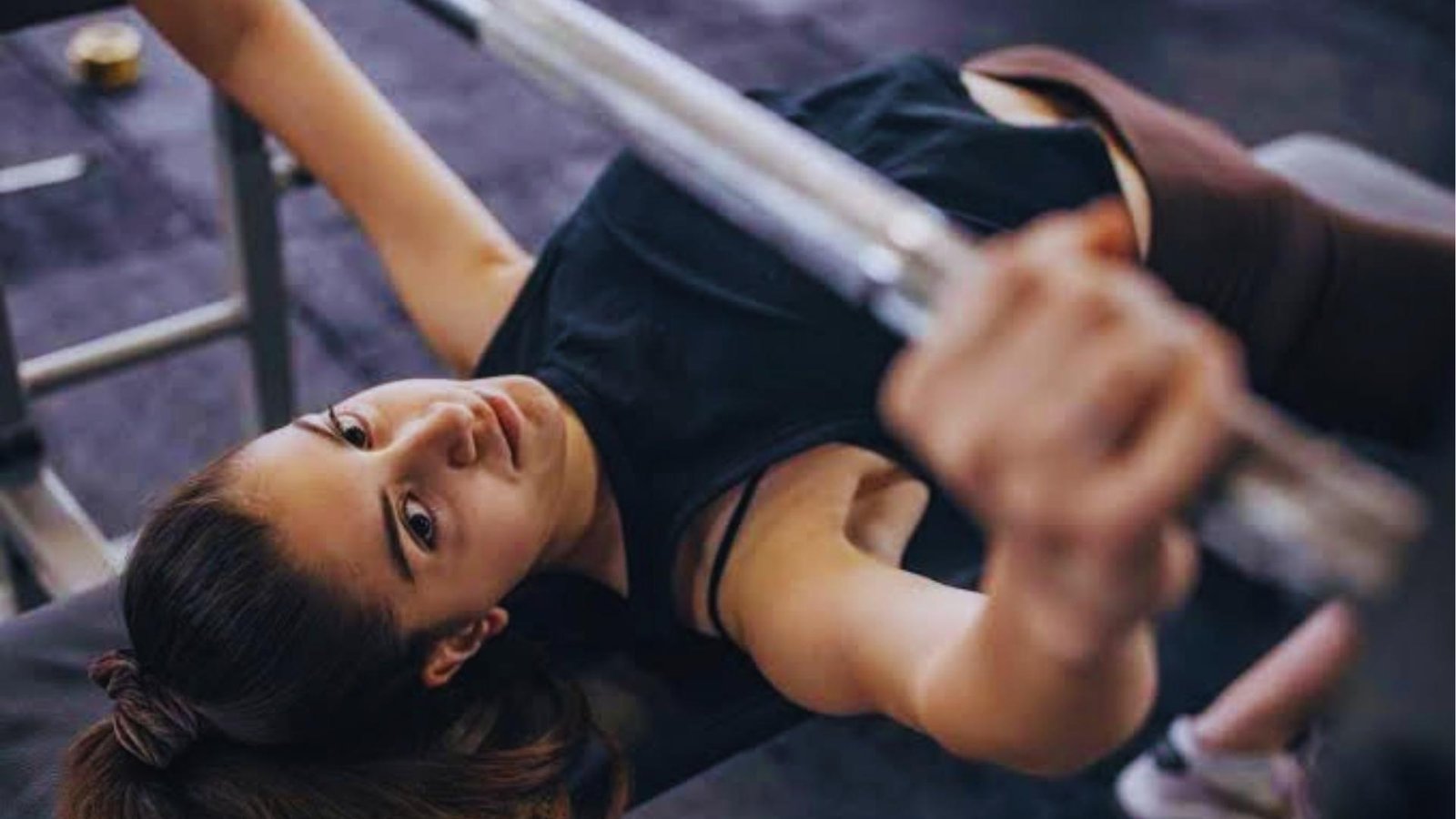 Woman doing barbell bench press in gym focusing on form to prevent shoulder pain causes.