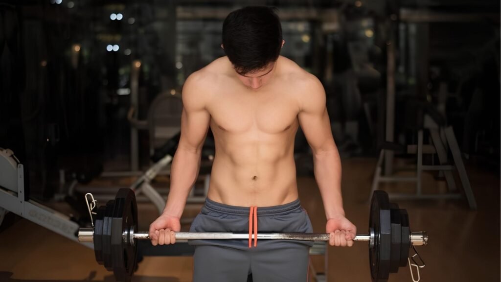 Shirtless man holding loaded barbell before bicep curl in gym, barbell curls exercise guide.