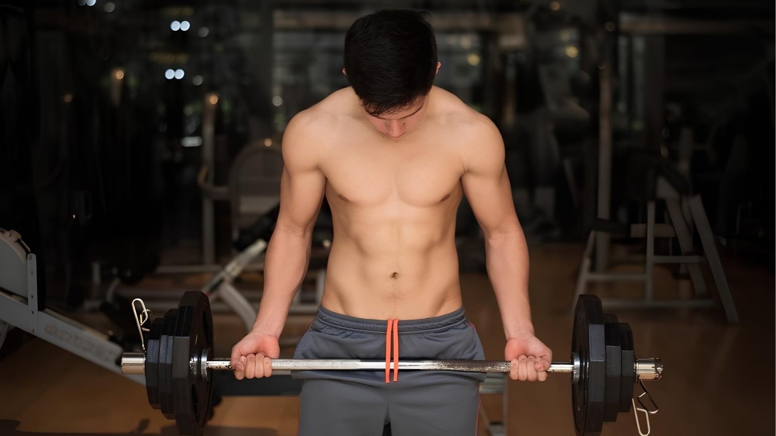Shirtless man holding loaded barbell before bicep curl in gym, barbell curls exercise guide.