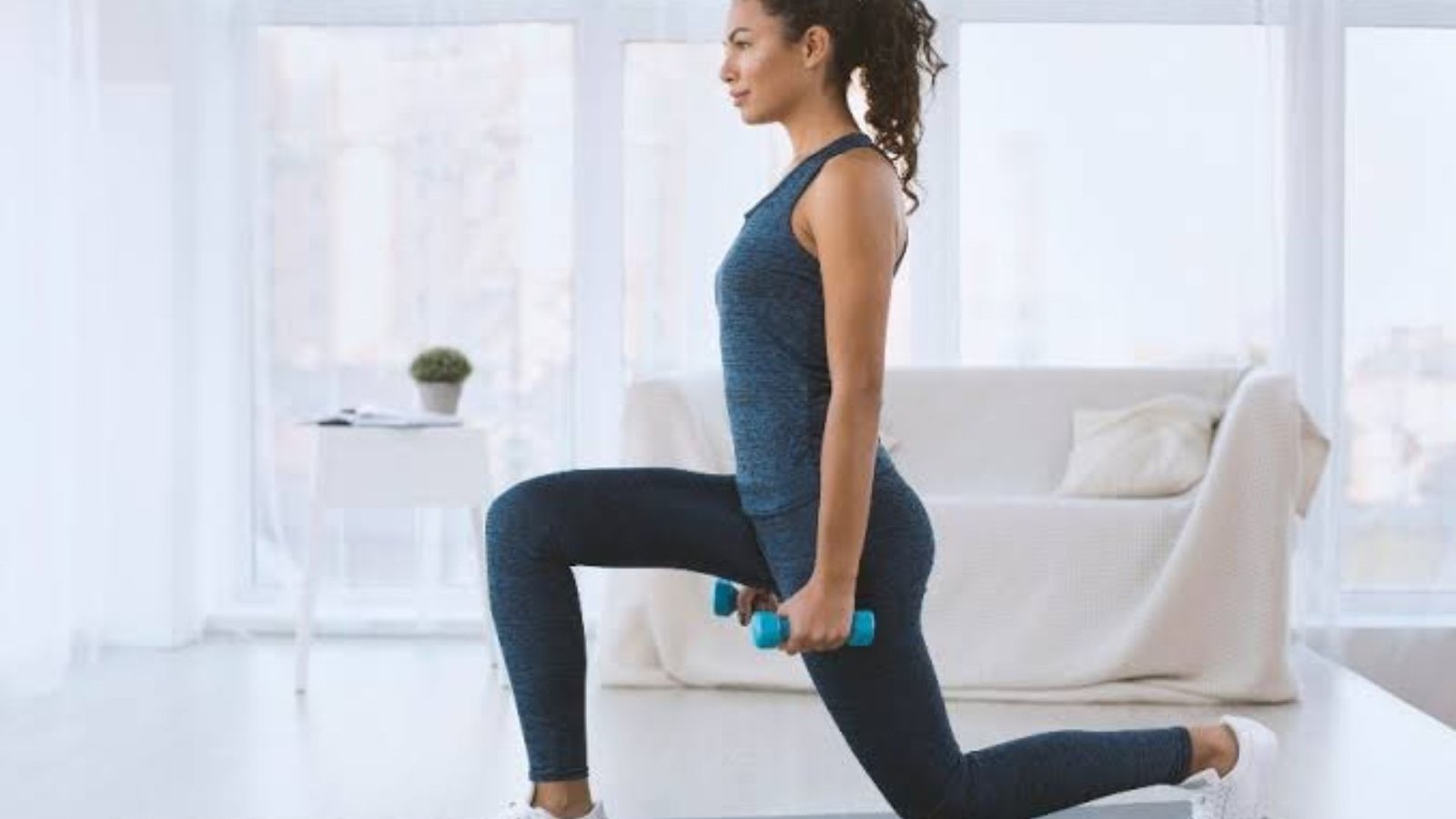 woman performing a dumbbell lunge at home as part of a weight loss workout.