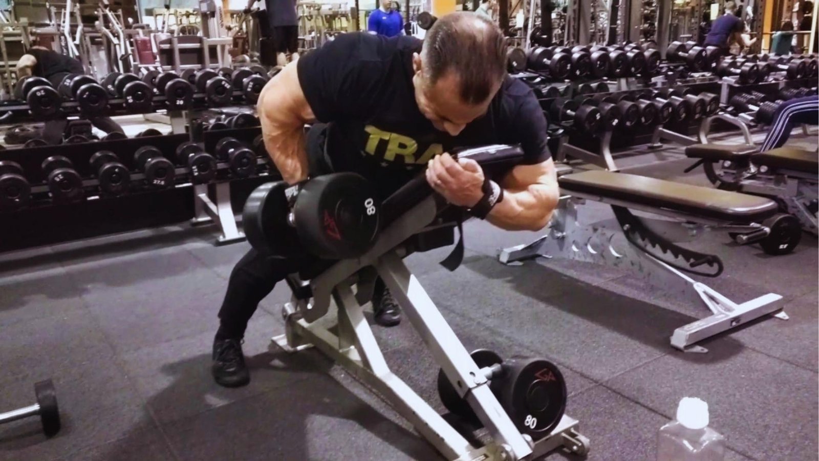 Bodybuilder doing single-arm dumbbell row on incline bench in gym, 80 lb dumbbell.