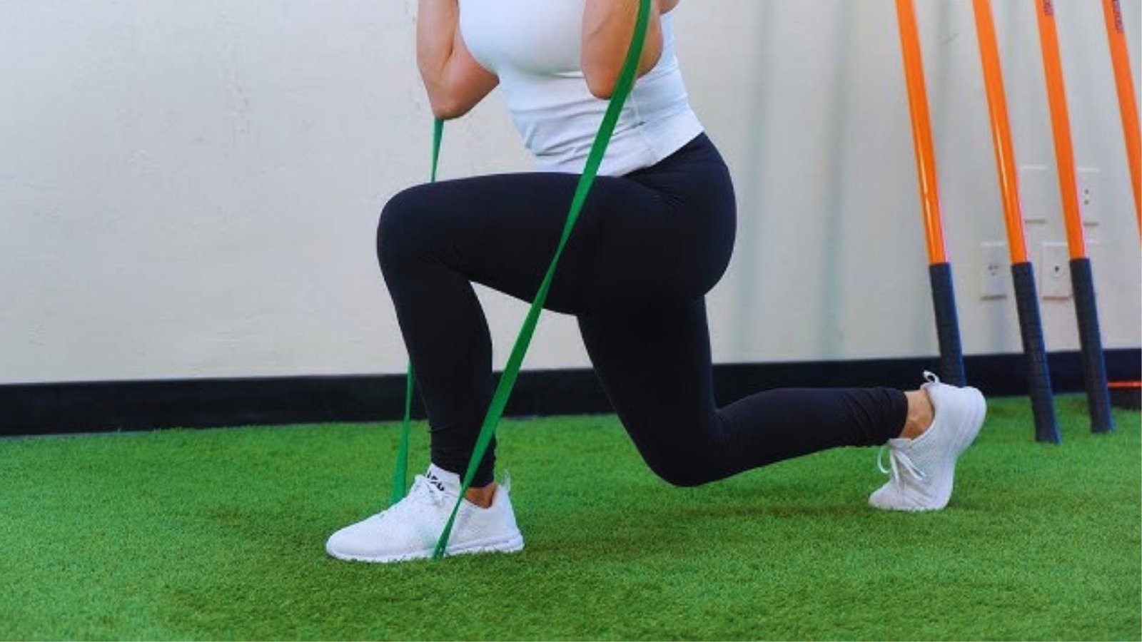 Woman performing front racked lunge with green long resistance band under foot, leg workout.
