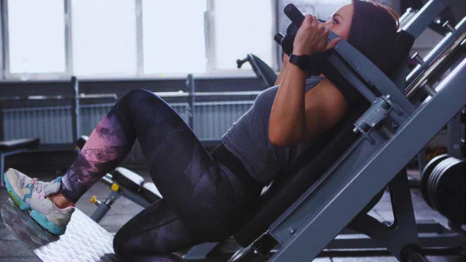 Woman in gym doing hack squat machine with shoulder pads, lower body strength training.