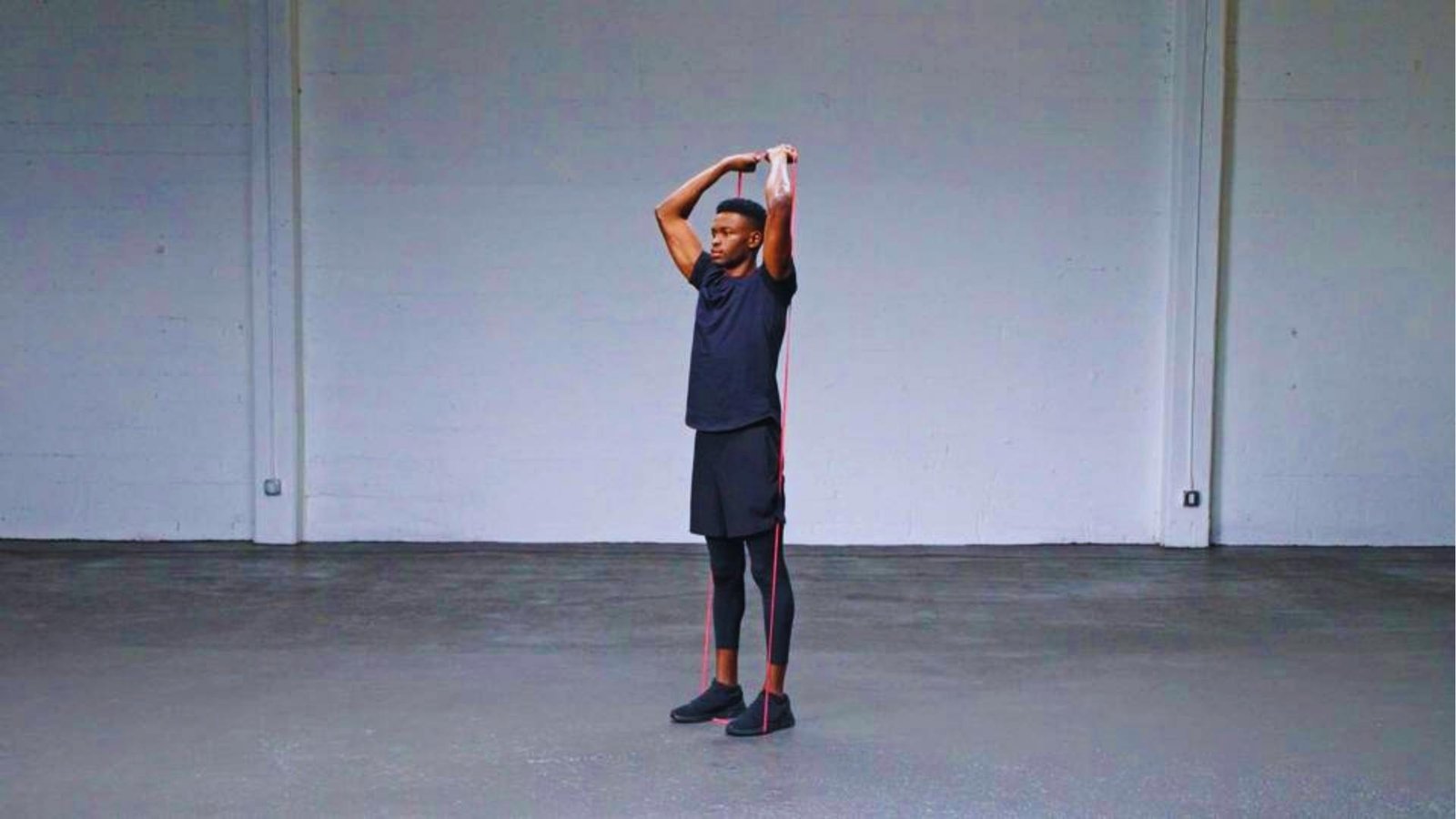Man doing overhead triceps extension with long red resistance band for arm workout.