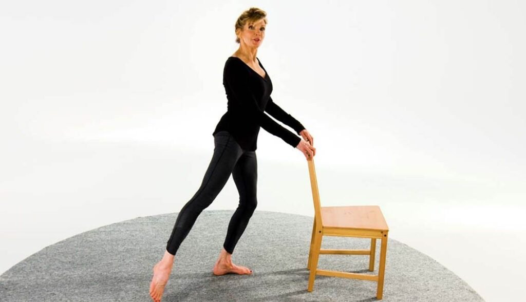 Woman performing barre exercises at home using a chair for a full body workout