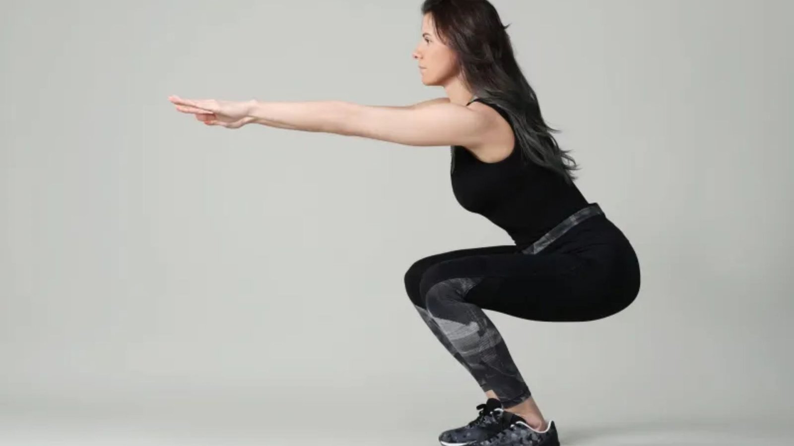 woman performing a bodyweight squat with arms extended to improve knee strength and quad activation.