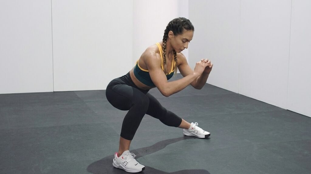 Woman with braids doing a lateral lunge in sports bra and leggings on gym floor.