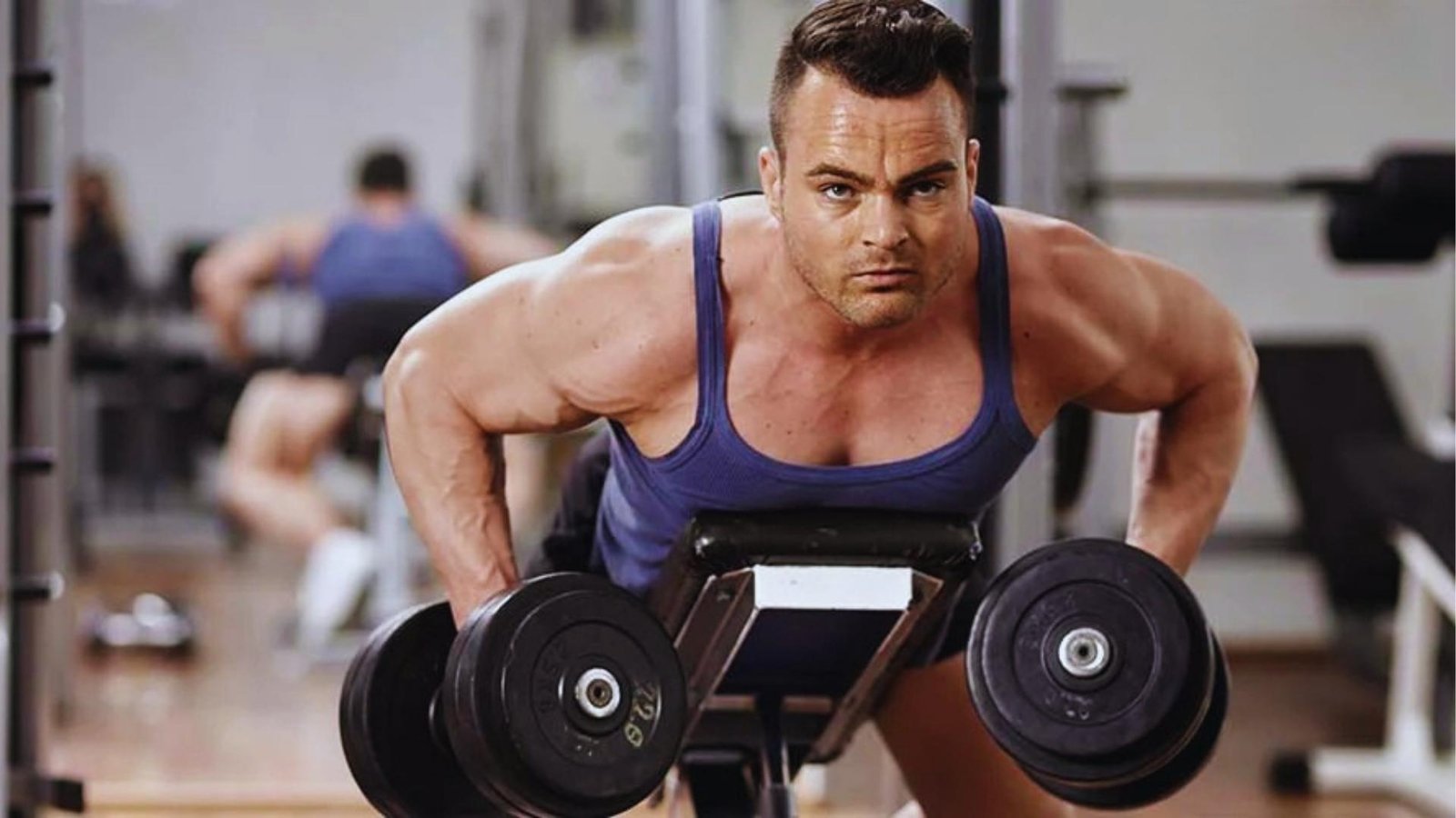 Muscular man performing heavy incline dumbbell chest supported row on bench for lats.
