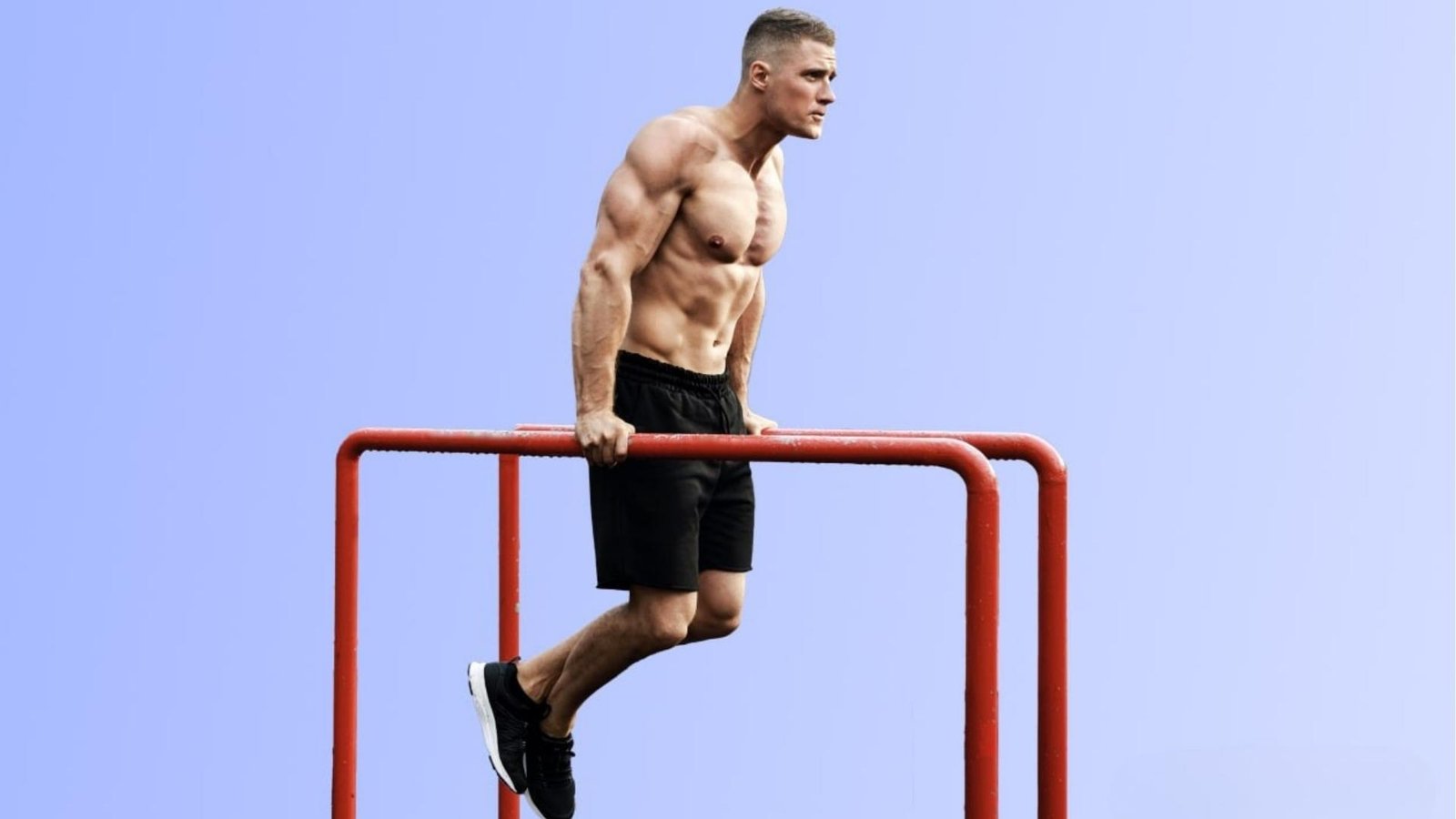 Fit man doing dips on red outdoor parallel bars, bodyweight chest and triceps exercise.