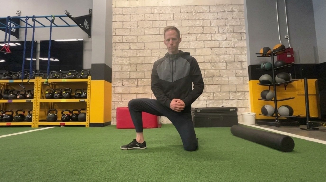 Man in black hoodie kneeling in a half kneeling lateral lunge on green gym turf.