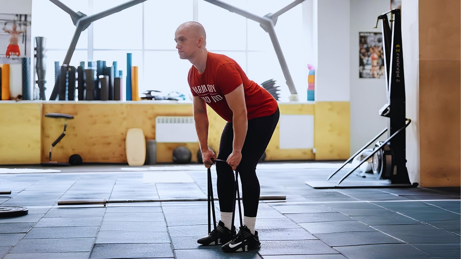 Man in red shirt doing resistance band deadlift row with black loop band under feet.
