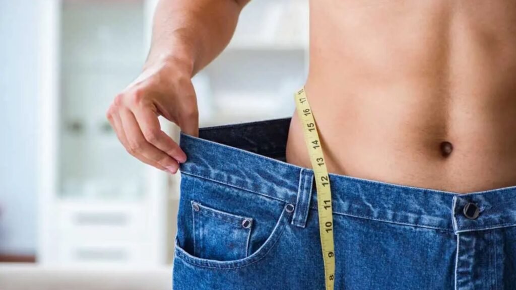 close-up of a man's waist with loose jeans and measuring tape after losing weight.