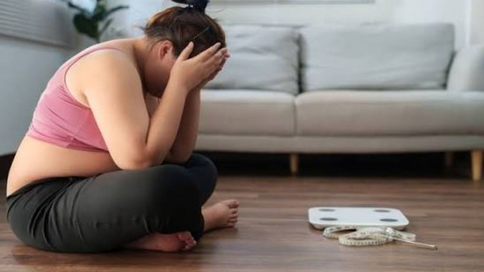woman feeling discouraged after a weigh-in beside a scale and measuring tape at home.