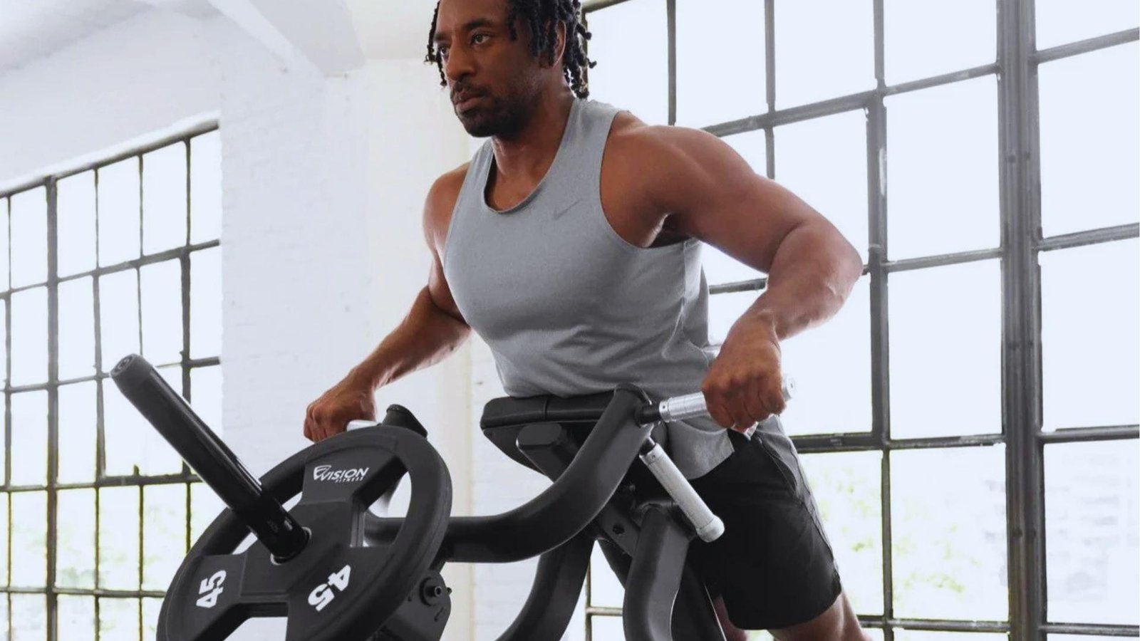 Athlete doing machine chest supported T-bar row with 45 lb plates in bright gym.